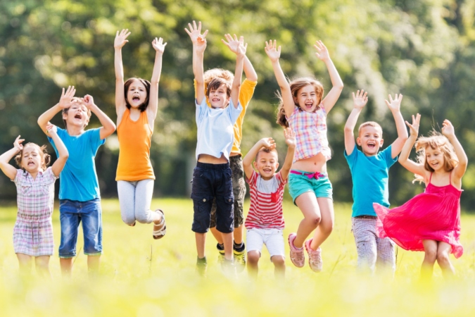 a group of children of different ages jumping in unison in a feld with their arms in the air