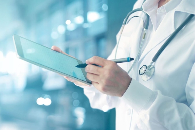 Clinician with Stethoscope holding ipad in hospital setting. Torso visible only.