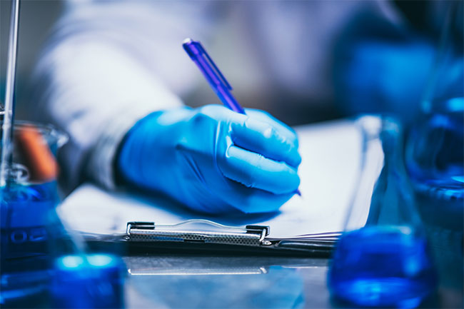 Clinician wearing blue gloves writing in a clipboard
